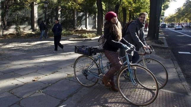 Dos madrileños circulan en bici por el Paseo del Prado
