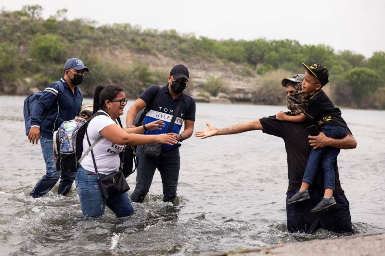 Una mujer intenta coger la mano de un compañero para poder cruzar el río