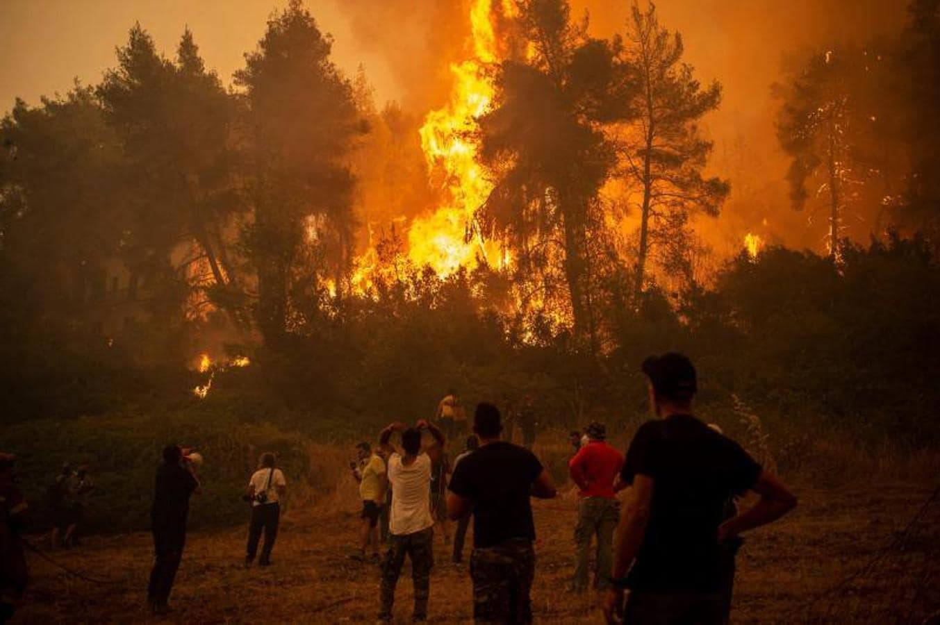 Un lugareño usa un megáfono para comunicarse con los bomberos mientras otros observan un gran incendio forestal que se acerca al pueblo de Pefki en la isla de Evia (Eubea)