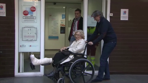 La alcaldesa Manuela Carmena sale del hospital en silla de ruedas y con el pie derecho escayolado ayudada por la edil Marta Higueras