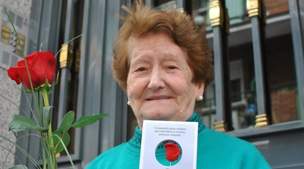 Una señora posa con la rosa de la campaña