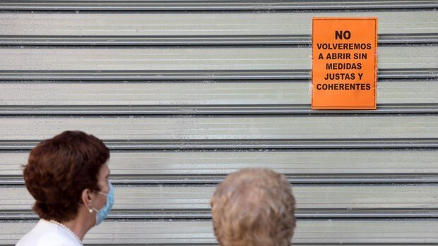 Dos mujeres leen un cartel puesto en una persiana echada de un comercio de Málaga