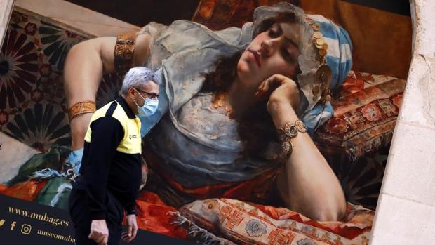 Un policía local alicantino pasa con mascarilla de protección junto al mural de una exposición de pintura, este viernes