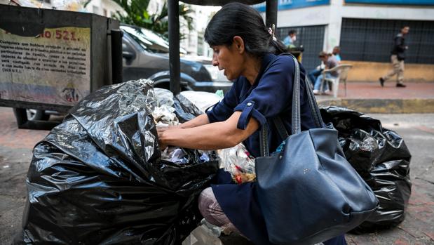una mujer mientras hurga en una basura en busca de comida en una calle de Caracas