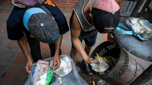 dos hombres mientras hurgan en una basura en busca de comida en una calle de Caracas en 2017