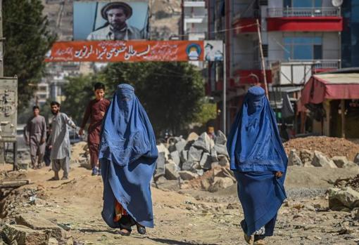Two women in burqa walk down a Kabul street in front of a sign with the image of the former Afghan commander Ahmad Shah Massoud