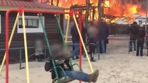 Un niño se columpia tranquilamente delante de un incendio