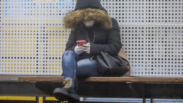 Imagen de una mujer consultando el móvil con guantes y mascarilla en Valencia