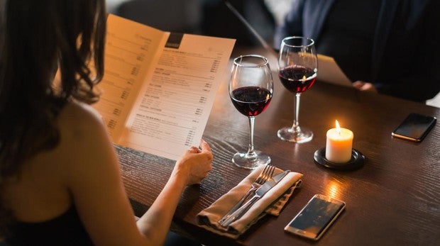 Una pareja examina la carta en un restaurante con dos copas de vinos sobre la mesa